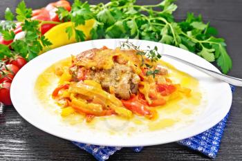 Chicken stewed with tomatoes, yellow and red bell peppers and cheese in white plate on a towel, thyme, parsley and garlic on black wooden board background