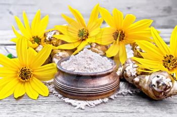 Jerusalem artichoke flour in a clay bowl on a burlap with flowers and vegetables on background of an old wooden board