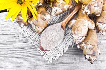 Jerusalem artichoke flour in a spoon on a burlap with flowers and vegetables on wooden board background from above
