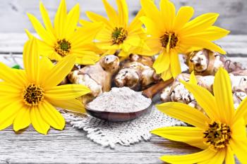Jerusalem artichoke flour in a spoon on a burlap with flowers and vegetables on wooden board background