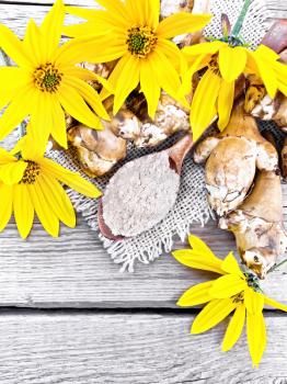 Jerusalem artichoke flour in a spoon on a burlap with yellow flowers and vegetables on wooden board background from above