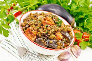 Green lentils stewed with eggplant, tomatoes, garlic and spices in a bowl on a towel, parsley on light wooden board background