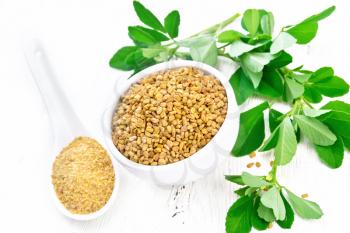 Fenugreek seeds in a bowl and ground spice in a spoon with leaves on wooden board background