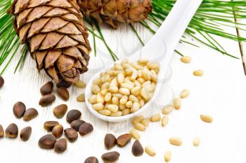 Peeled kernels of cedar nuts in a spoon, two pinecones and nuts in the shell against a light wooden board
