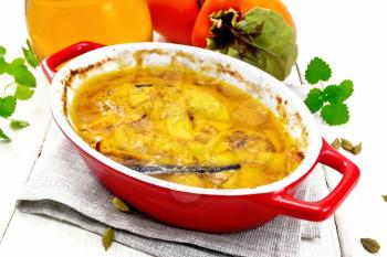 Persimmon baked with honey, cardamom and vanilla in a roasting pan on a towel, mint and orange fruit on white wooden board background