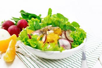 Radish, onion and orange salad with mint, vegetable oil and spices on lettuce in a plate on a napkin on the background of light wooden board