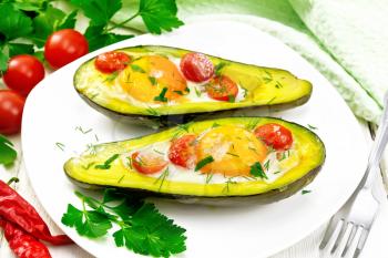 Scrambled eggs with cherry tomatoes in two halves of avocado in a plate, napkin and fork on white wooden board background