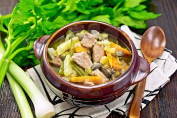 Eintopf soup made from pork, celery, beans, carrots and potatoes with leek in a clay bowl on a napkin on dark wooden board background