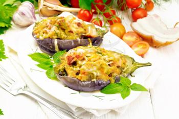 Stuffed eggplant with smoked bacon, tomatoes, onions, carrots with garlic, cheese and herbs in an oval plate on a napkin on wooden board background