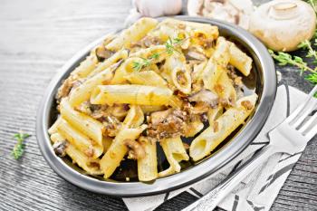 Penne pasta with wild mushrooms in a plate on a kitchen towel, thyme, fork and garlic on wooden board background