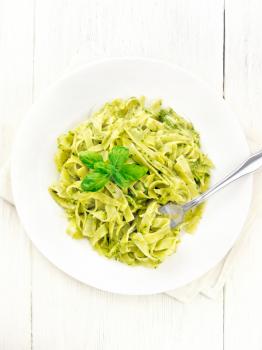 Tagliatelle pasta with pesto, basil and fork in a plate on a napkin against the background of light wooden board on top