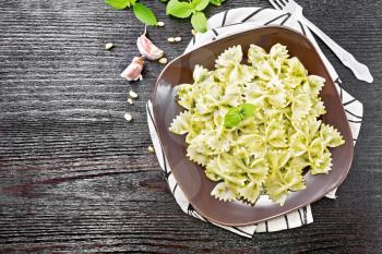 Farfalle pasta with pesto, basil in a plate on a towel on wooden board background from above