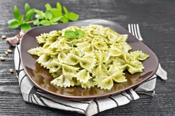Farfalle pasta with pesto, basil in a plate on a towel on wooden board background