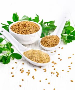 Ground fenugreek in a spoon, spice seeds in a bowl and spoon with green leaves on wooden board background