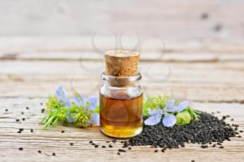 Nigella sativa oil in a bottle, seeds and twigs of black caraway seeds with blue flowers and green leaves of kalingi on a wooden board background