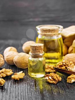 Walnut oil in a glass bottle and a jar, nuts in jute bag, spoon and on table on wooden board background