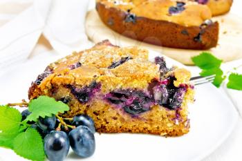 Piece of sweet cake with black grapes and honey, mint and a fork in a plate, a napkin on light wooden board background