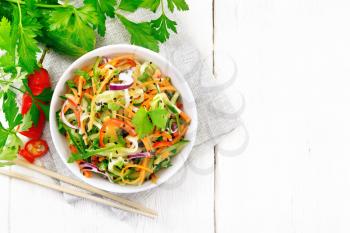 Spicy salad of cucumbers, carrots, chili peppers, purple onions, cilantro and black sesame, seasoned with vinegar and lemon juice in a bowl on a napkin on wooden board background from above