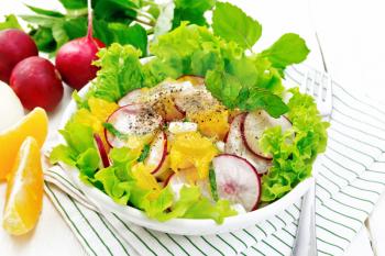 Radish, onion and orange salad with mint, vegetable oil and spices on lettuce in a plate on a napkin on white wooden board background