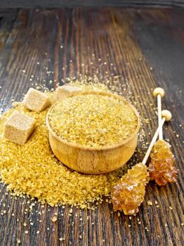 Granulated brown sugar in a bowl and on a table, crystalline on a stick and sugar cubes on wooden board background