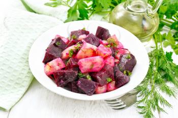 Salad of beets and potatoes, seasoned with vegetable oil and vinegar in a plate, napkin, fork, parsley and dill on the background of light wooden boards