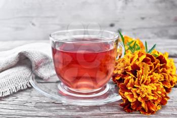 Marigold herbal tea in a glass cup and saucer, fresh flowers, burlap on wooden board background