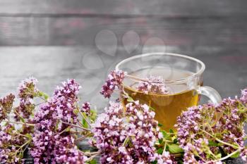 Oregano herbal tea in a glass cup, fresh pink marjoram flowers on dark wooden board background