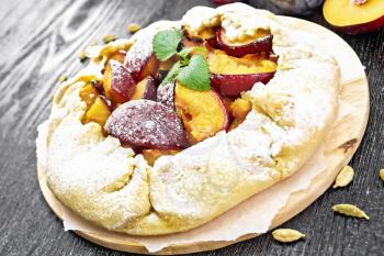 Sweet pie with plum, sugar and cardamom on paper, sprigs of green mint on a wooden board background