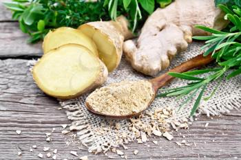 Ground ginger in a spoon, flakes and ginger root on burlap, spicy herbs on a background of an old wooden board