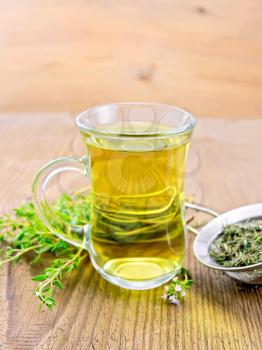 Herbal tea in a glass mug of thyme, metal strainer with dry leaves, a bunch of fresh savory on the background of an old wooden board