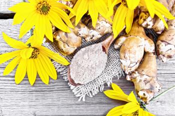 Jerusalem artichoke flour in a spoon on a burlap with flowers and vegetables on background of an old wooden board from above