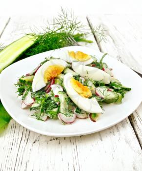 Salad from radish, cucumber, sorrel, greens and eggs, dressed with mayonnaise and sour cream in a plate on the background of a wooden table