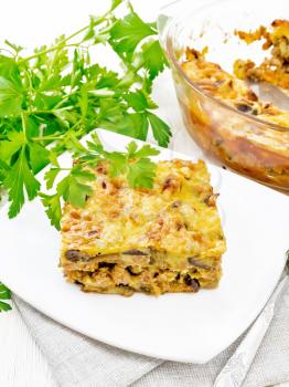 Casserole of minced meat, onion and eggplant doused with a sauce of eggs, milk, cheese and flour in a plate on napkin against wooden board background