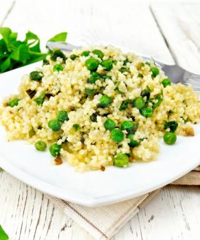 Couscous with spinach and green peas in a plate on a towel, basil and fork basil and fork on a light wooden board background
