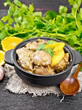 Chicken liver stewed with oranges, sour cream, soy sauce and Provence herbs in a small saucepan on burlap, a spoon and parsley on a dark wooden board background