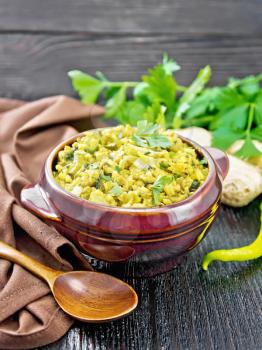 Indian national dish kichari made of mung bean, rice, celery, spinach, hot pepper and spices in a bowl on a towel, ginger and spoon on black wooden board background