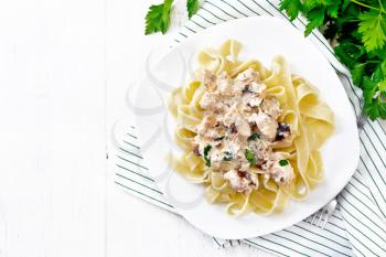 Tagliatelle pasta with salmon, cream, garlic and herbs in a plate on a towel, fork, parsley and basil on wooden board background from above