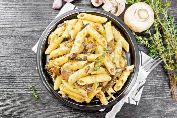 Penne pasta with wild mushrooms in a plate on a towel, thyme, fork and garlic on wooden board background from above
