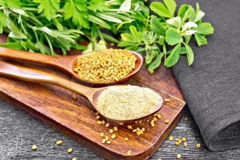 Fenugreek seeds and ground spice in two spoons on a brown plate with herbs, a napkin on wooden board background