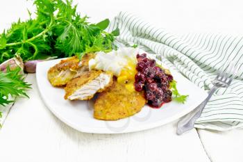Fried turkey breast in breadcrumbs with cranberry sauce, boiled egg, baked parsnip and lettuce in a plate, towel and fork on light wooden board background