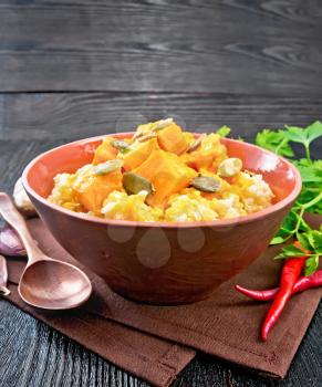 Millet porridge with spicy pumpkin sauce and seeds in a clay bowl on a napkin, hot pepper, ginger root, garlic and parsley on wooden board background