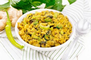 Indian national dish of kichari made of mung bean, rice, stalk celery, spinach, hot pepper and spices in a bowl on napkin, ginger on white wooden board background