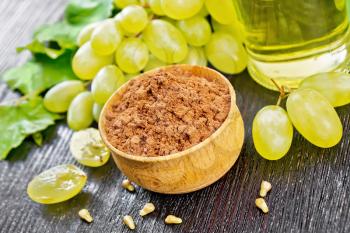 Grape seed flour in a bowl, oil in a jar and green grapes on dark wooden board background
