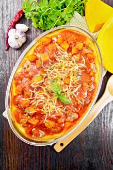 Corn porridge with meatballs, sauce of tomato, garlic and pumpkin, sprinkled with cheese, basil in a pan on towel on wooden board background from above
