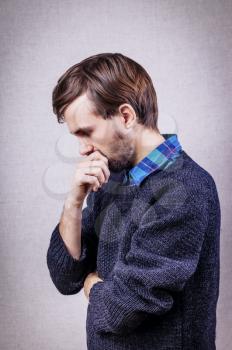 young man with a beard in blue sweater thinking with hand on face