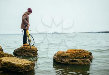 a young man with a bicycle stands on stone in lake