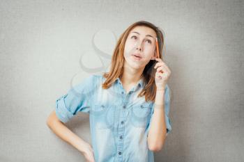 woman thinks pencil near the face. isolated on gray background