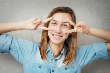 Young woman watching through fingers victory glasses over a grey background