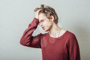 The man in glasses upset sad, hand on his head, his head lowered. On a gray background.