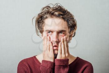 Closeup portrait, headshot young tired, fatigued business man worried, stressed, dragging face down with hands, isolated , grey background. Negative human emotions, facial expressions, feelings